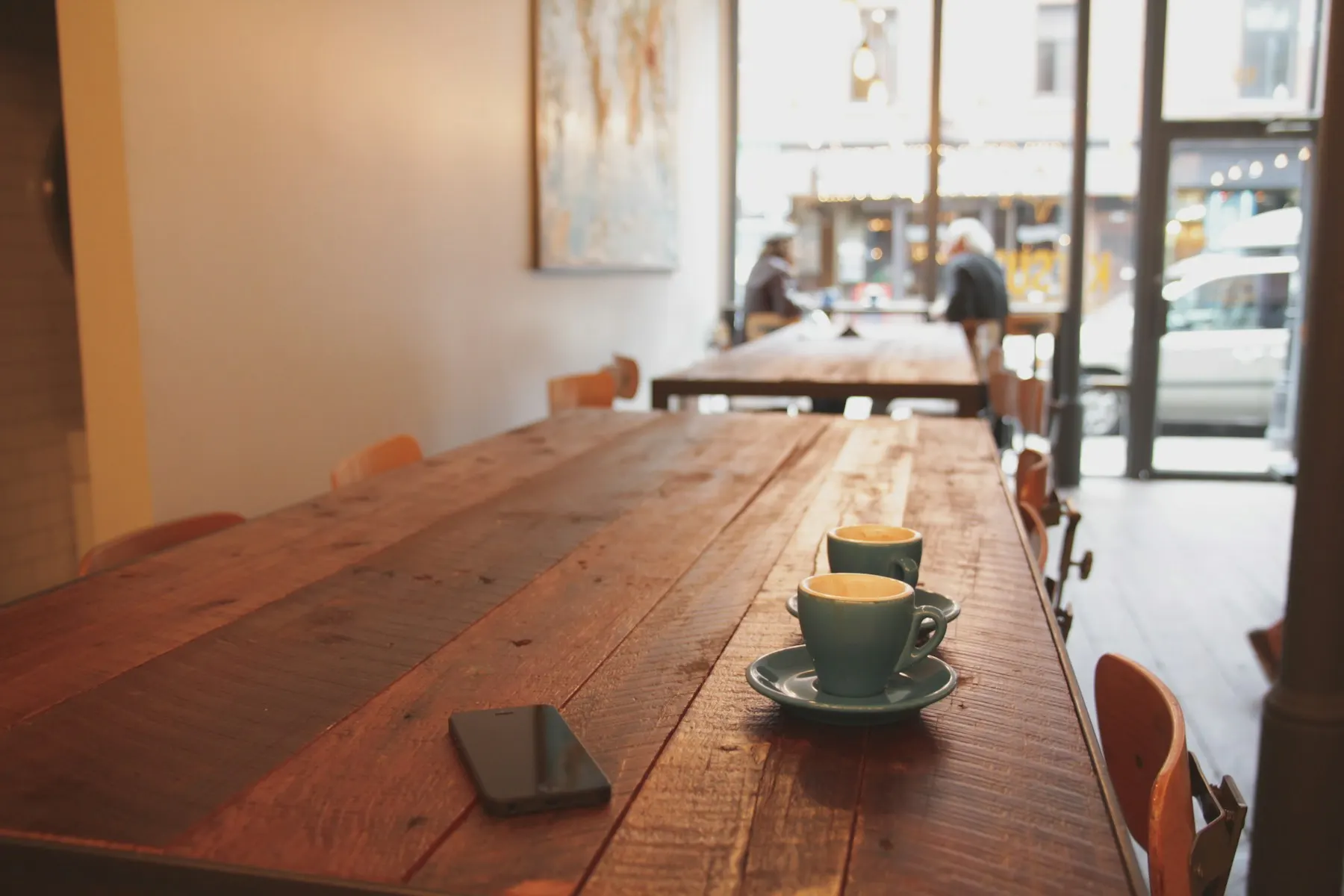 A long wooden café table by sunlit windows